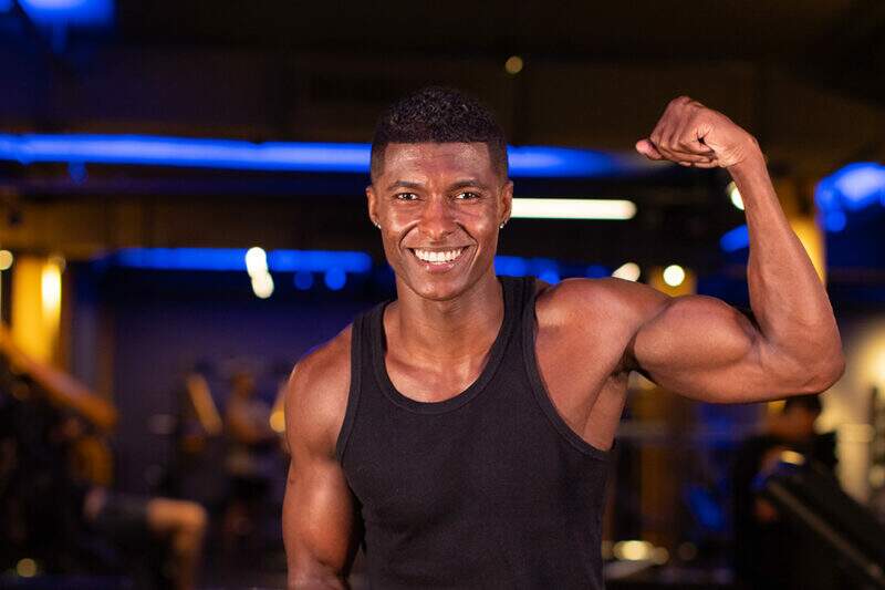 Homem musculoso sorrindo para a câmera e flexionando o bíceps