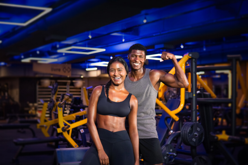 A imagem apresenta duas pessoas em uma unidade da Smart Fit, sorrindo para a foto.