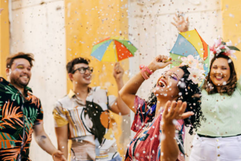 A imagem apresenta quatro pessoas se divertindo no carnaval, com confetes caindo sobre elas.